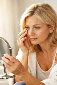 Woman noticing under-eye puffiness while looking in the mirror in soft morning light