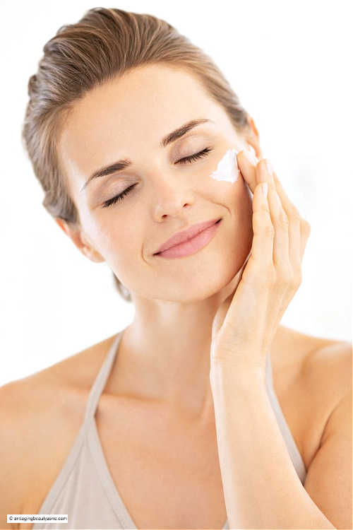 Woman applying antioxidant facial moisturizer to her cheek, showing proper application for different skin types