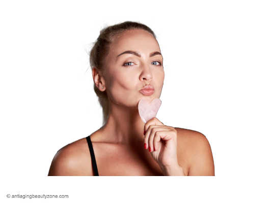 Woman with sculpted facial contours using a gua sha tool under her chin to reduce puffiness and support lymphatic drainage.