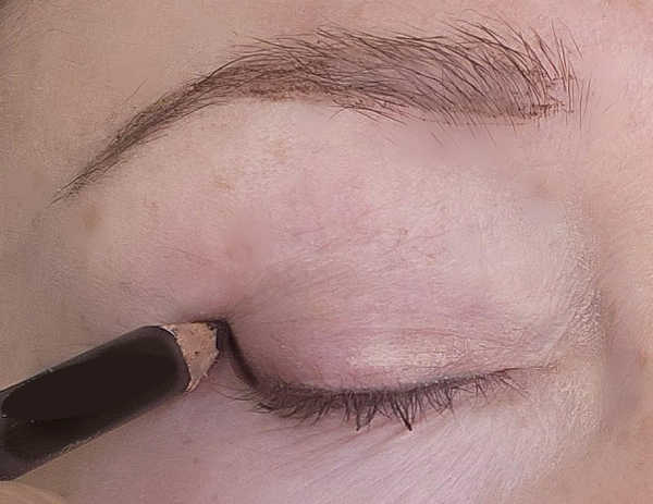 Drawing a tiny upward eyeliner flick on a mature hooded eye with the eye closed