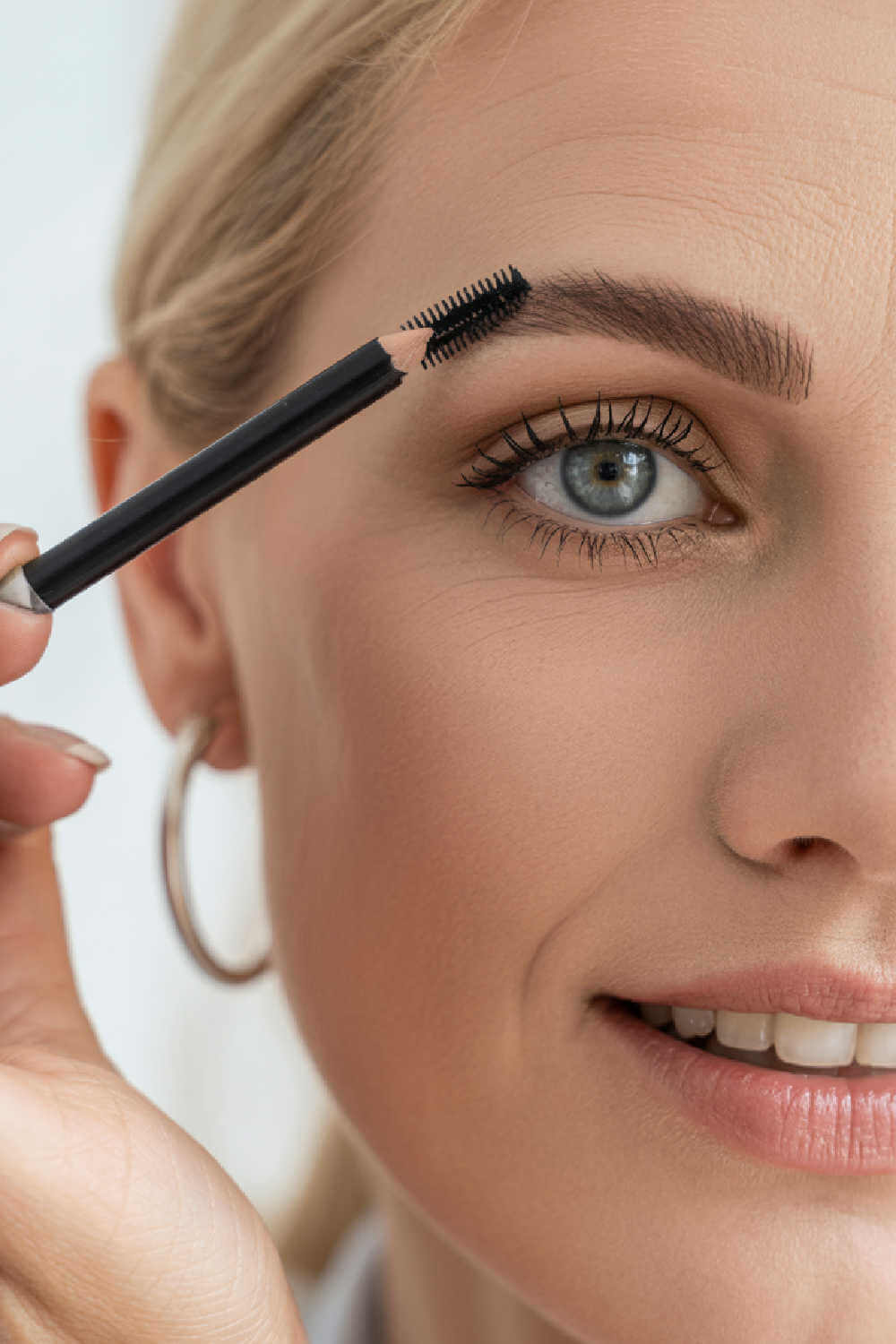 Woman over 40 brushing and shaping thin eyebrows with a brow spoolie for a fuller, defined look