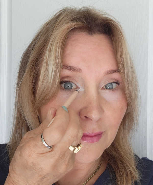 Light concealer applied in a small greater-than shape at the inner corner of the eye and blended to brighten dark circles.