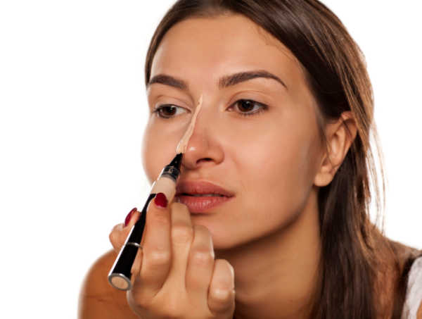 Using nose highlighting to reduce dark circles and enhance brightness. Woman applying highlighter to the bridge of her nose to brighten the under-eye area.