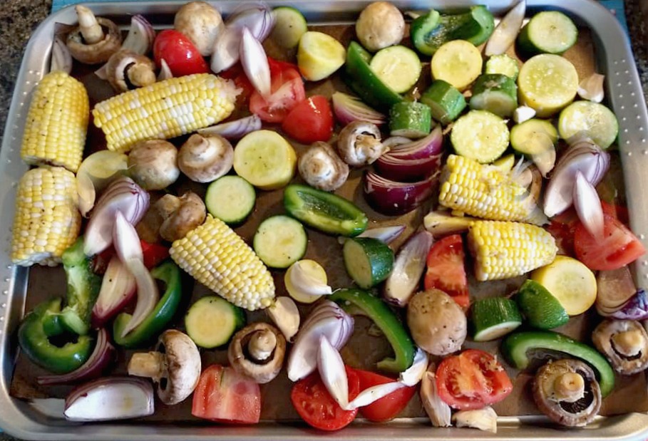 How I prep skin-friendly roasted veggies for the week—loaded with sulfur-rich and antioxidant-packed ingredients. Tray of chopped vegetables ready for roasting, including garlic, onions, zucchini, corn, tomatoes, and mushrooms—skin-nourishing foods that support healthy, glowing skin.